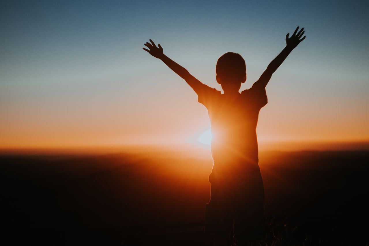 A child with arms raised toward the sunrise